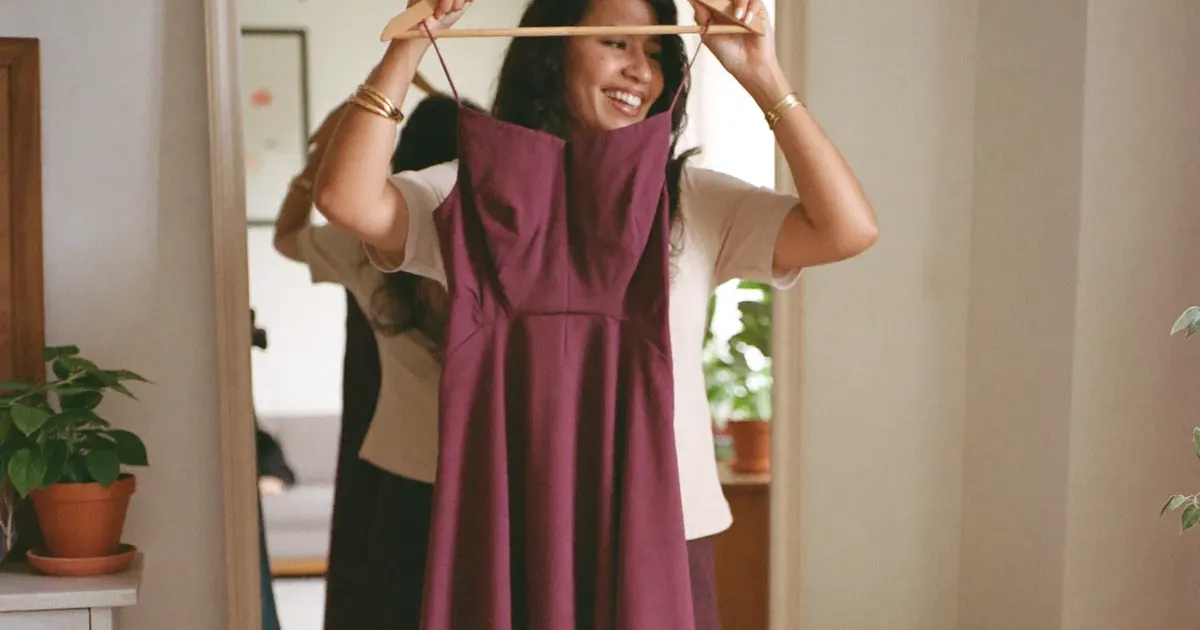 Woman holding up a burgundy midi dress she is getting ready to sell online in Canada